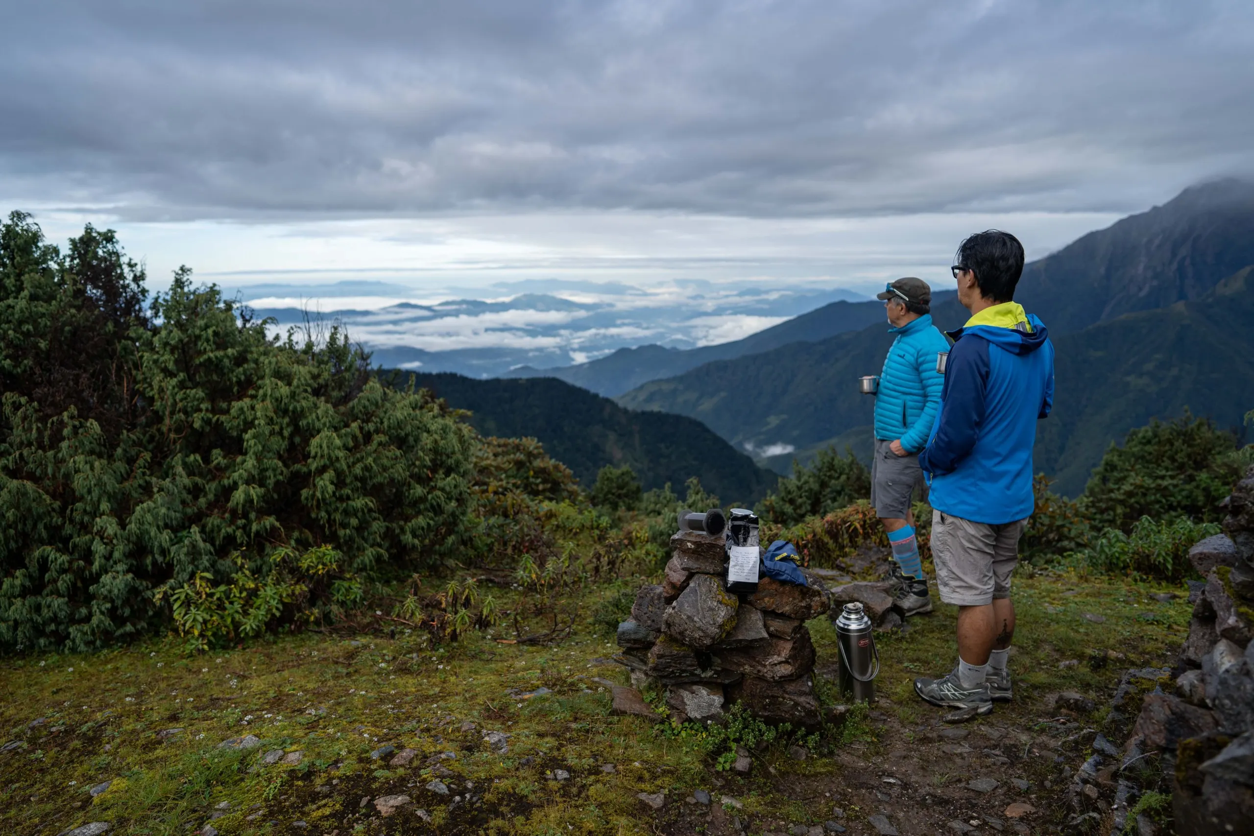 Two trekkers on a grassy ridge above a sea of cloud in the Helambu hills
